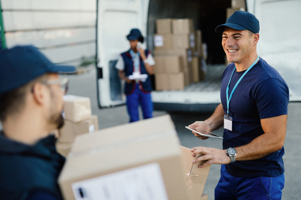 Happy manual worker using touchpad while communicating with his coworker and organizing package delivery. Custom clearance agent in Dubai
